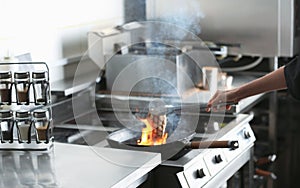 Female chef cooking meat with burning flame on stove in restaurant kitchen