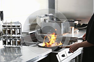 Female chef cooking meat with flame on stove in restaurant kitchen, closeup