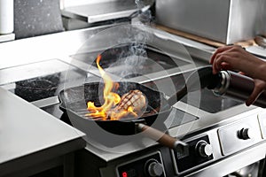 Female chef cooking meat with manual gas burner on stove in restaurant kitchen