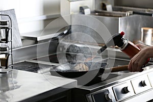 Female chef cooking meat with manual gas burner on stove in restaurant kitchen