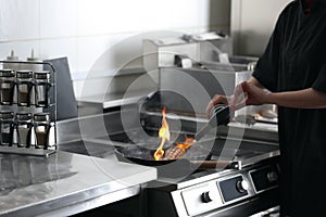 Female chef cooking meat with manual gas burner on stove in restaurant kitchen, closeup