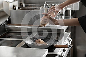 Female chef cooking meat on stove in restaurant kitchen, closeup