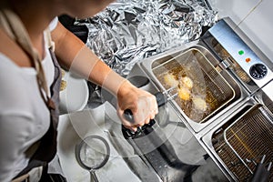 Female chef deep-frying meat in a professional kitchen.