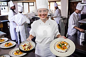 Female chef holding plate of prepared pasta in kitchen