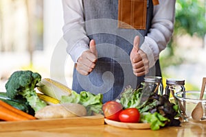 A female chef making and showing thumbs up hand sign while preparing fresh mixed vegetables to cook in kitchen