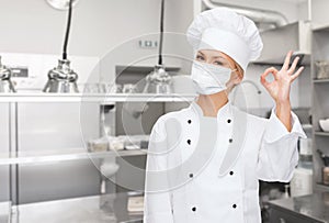 Female chef in mask showing ok sign at kitchen