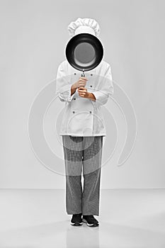 female chef peeking out from behind frying pan