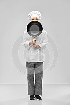 female chef peeking out from behind frying pan