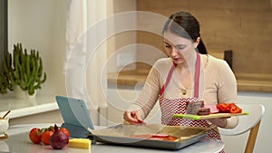 Female chef preparing a pizza and watching recipes online on platform for watching videos on your tablet