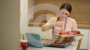 Female chef preparing a pizza and watching recipes online on platform for watching videos on your tablet