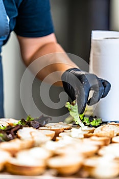 Female Chef Putting Ingredients of Burgers on a Sliced Bread Spread on a Table in Black Gloves - Concept of the Hard Working