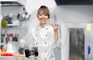 female chef with saucepan tasting food on kitchen