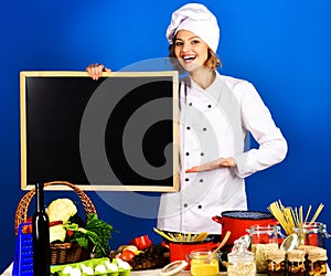 Female chef with vegetables at table holding blank menu blackboard. Beautiful woman chef with blank blackboard. Cook in
