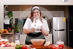 Female chef in white chef coat sifting flour for bakery or pizza.