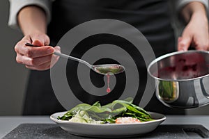 A female chef in a white uniform and a black apron in the restaurant kitchen. The cook pours red cranberry salad sauce