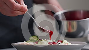 A female chef in a white uniform and a black apron in the restaurant kitchen. The cook pours red cranberry salad sauce