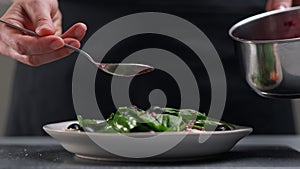 A female chef in a white uniform and a black apron in the restaurant kitchen. The cook pours red cranberry salad sauce