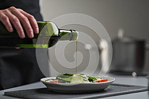 A female chef in a white uniform and a black apron in the restaurant kitchen. Cooking. The cook pours olive oil from a