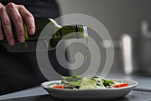 A female chef in a white uniform and a black apron in the restaurant kitchen. Cooking. The cook pours olive oil from a