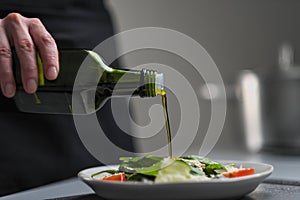A female chef in a white uniform and a black apron in the restaurant kitchen. Cooking. The cook pours olive oil from a