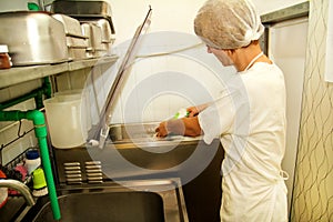 Female chef and worker is working at ice cream factory is pouring pasteurized milk and cooking mixing milk.