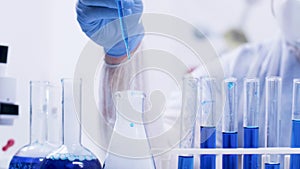 Female chemical scientist in a modern laboratory pouring reagent with pipette from test tubes with blue liquid