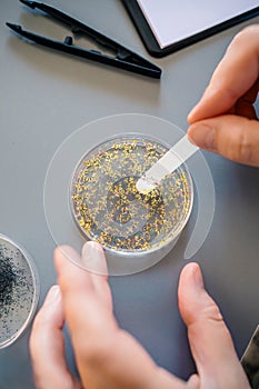 Female chemist hands taking sample of microplastics from golden glitter on petri dish in laboratory photo