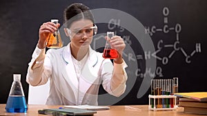 Female chemist looking at colored liquids in flasks, developing new substance