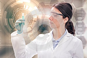 Female chemist wearing lab coat and protective eyeglasses holds a test-tube in abstract backdrop