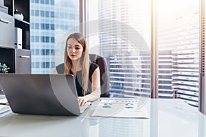 Female chief executive sitting at her desk taking notes in datebook writing with pen and using her computer in modern