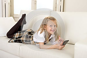 Female child with blond hair lying on home sofa using internet app on mobile phone