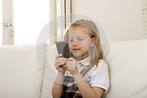 Female child with blond hair sitting on couch using internet app on mobile phone