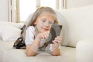 Female child with blond hair sitting on couch using internet app on mobile phone