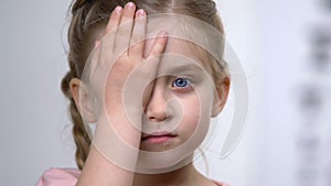 Female child covering eye with hand, ophthalmological exam, nearsightedness