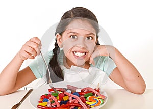 Female child eating dish full of candy in sugar excess and sweet nutrition abuse photo