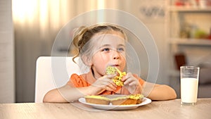 Female child eating tasty donut, milk glass on table, sweet snack, nutrition