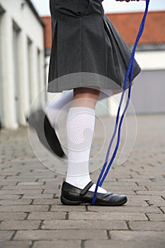 Female child with grey skirt, shot side on from the waist down while skipping with a blue skipping rope, on cobbles