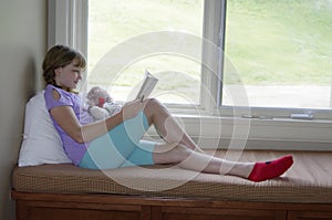 Female child reading a book on a window seat in summer