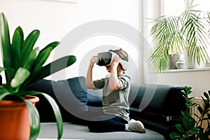 Female child watching video or playing game with the help of black-white 3D Virtual Reality glasses sitting on sofa