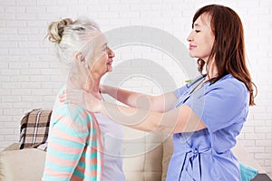 Female chiropractor looking at senior woman with neck pain in the medical office or home