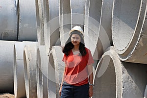 Female civil engineer or architect wear the white helmet standing on background of large cement pipes stacked