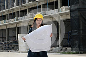 Female civil engineer or architect with yellow helmet, standing with project drafts while in hand