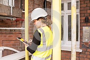 Female civil engineer taking notes on her tablet with electronic pen during a survey, hard hat and yellow high visibility vest