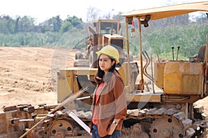 Female civil engineer with yellow helmet standing and turn sideways with Bulldozer Truck with Front Loader Truck Engineering