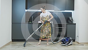 Female cleaning kitchen using vacuum cleaner. Young woman cleaning house and having fun. Happy girl vacuuming in the kitchen of ho