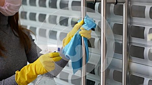 Female cleaning lady, in protective mask and gloves, wipes door handles with antiseptic in restaurant or public