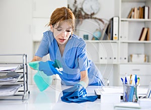 Female cleaning service worker wiping working table in office
