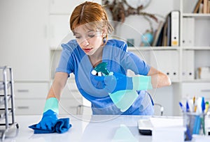 Female cleaning service worker wiping working table in office