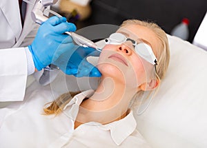 Female client receiving face skin laser resurfacing at cosmetology clinic