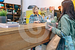 Female client taking credit card to pay purchased items while talking with woman employee on store